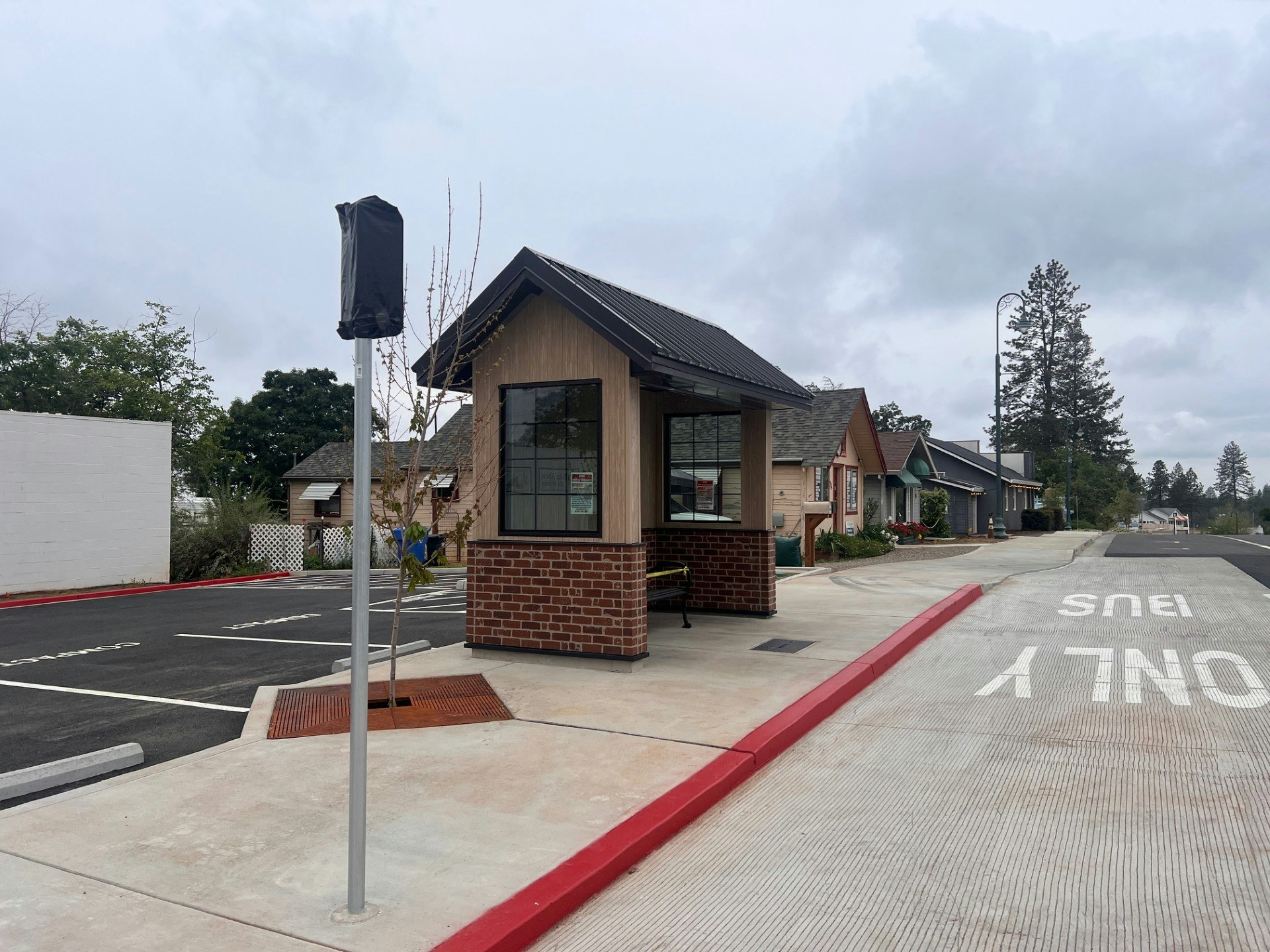 The image shows a small building with a service window, surrounded by parking spaces and residential homes in a neighborhood setting.