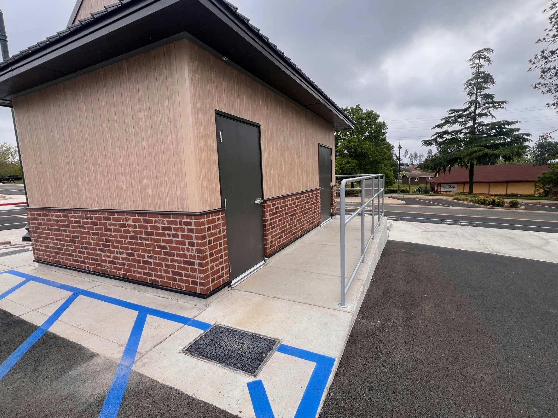 A building corner with a door and railing, gray clouds above, and a paved area with blue lines for parking.