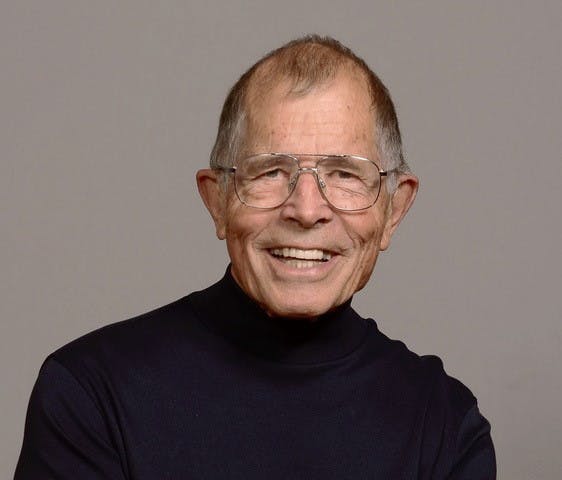 A smiling elderly man with glasses, wearing a black turtleneck.