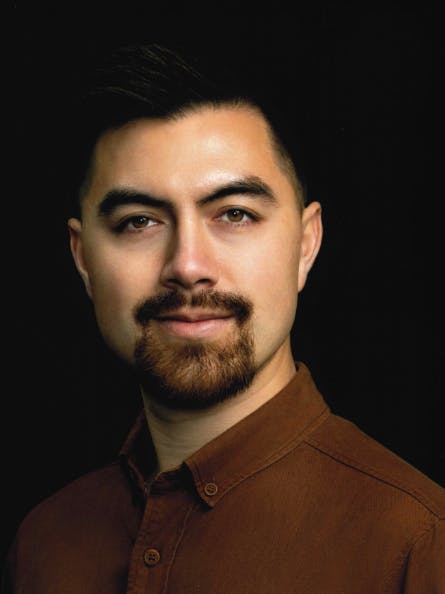 A portrait of a man with a mustache, wearing a brown shirt, against a black background.