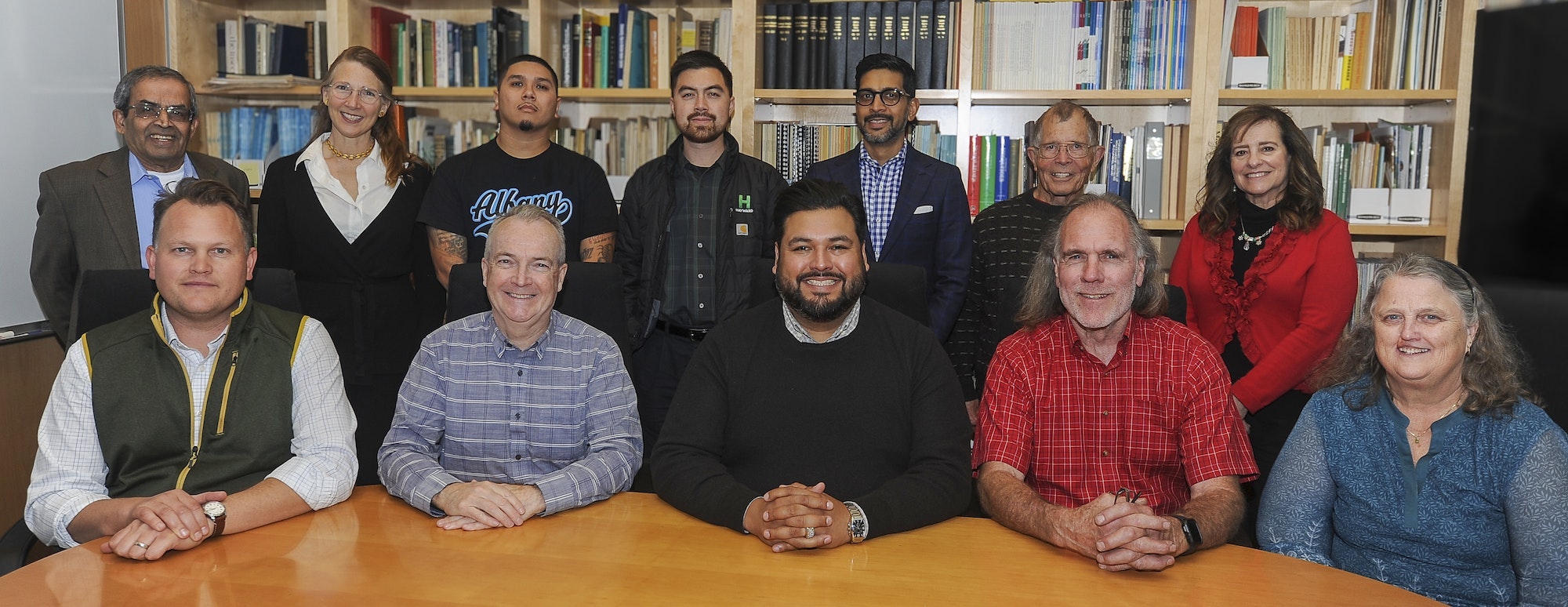 A diverse group of people poses together at a table, with bookshelves in the background, likely for a meeting or photo opportunity.