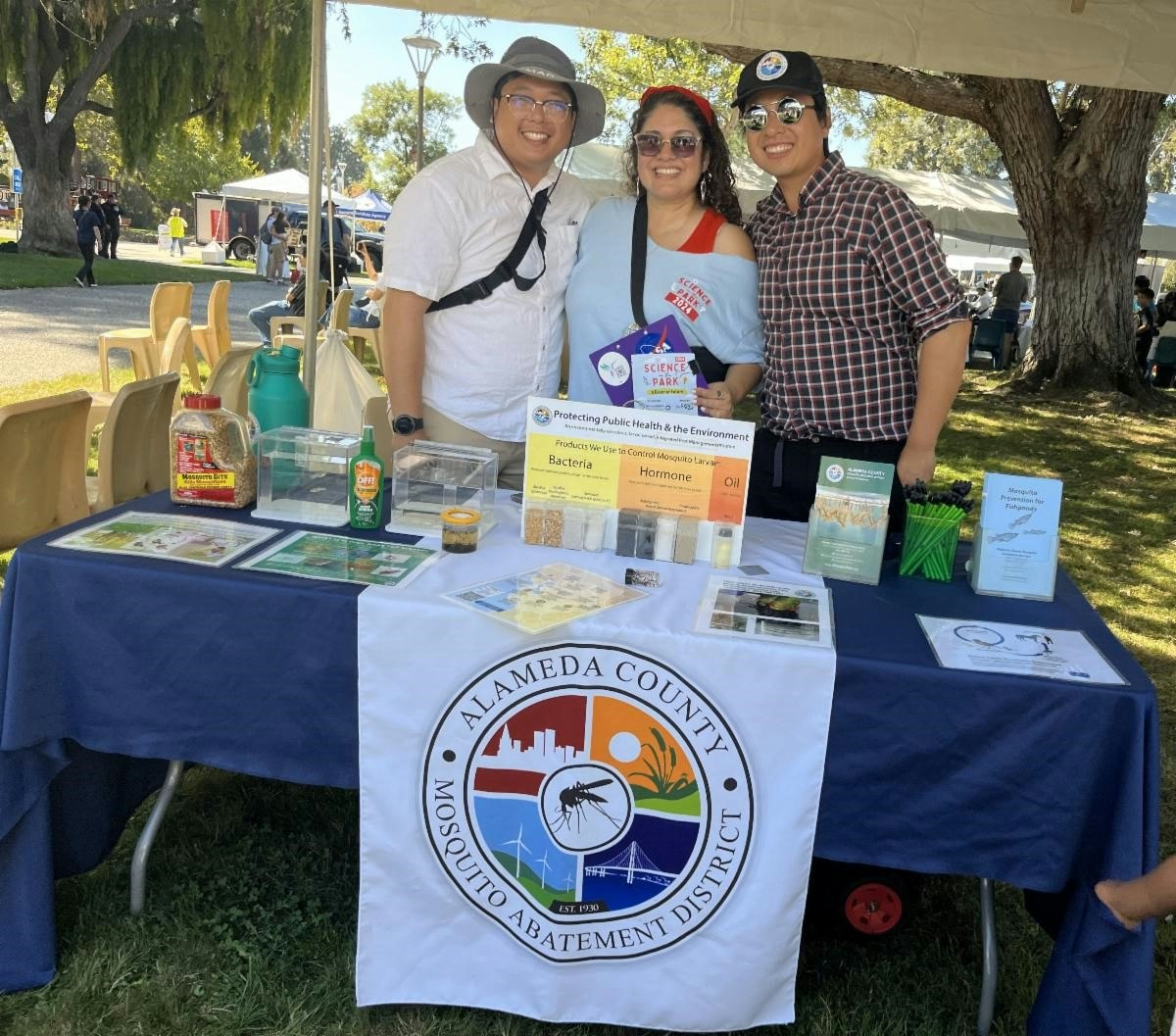 Three people posing behind a booth with educational materials for Alameda County Mosquito Abatement District.