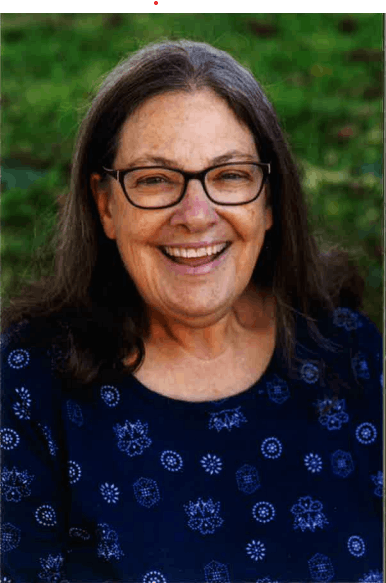 A smiling woman wearing glasses and a blue top with a green background.