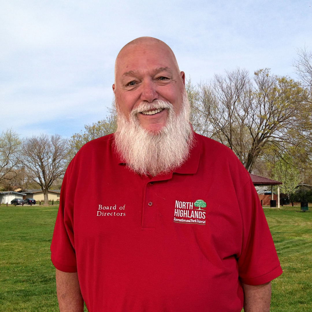 A person in a red "North Highlands Recreation and Park District" polo shirt stands outdoors, smiling.