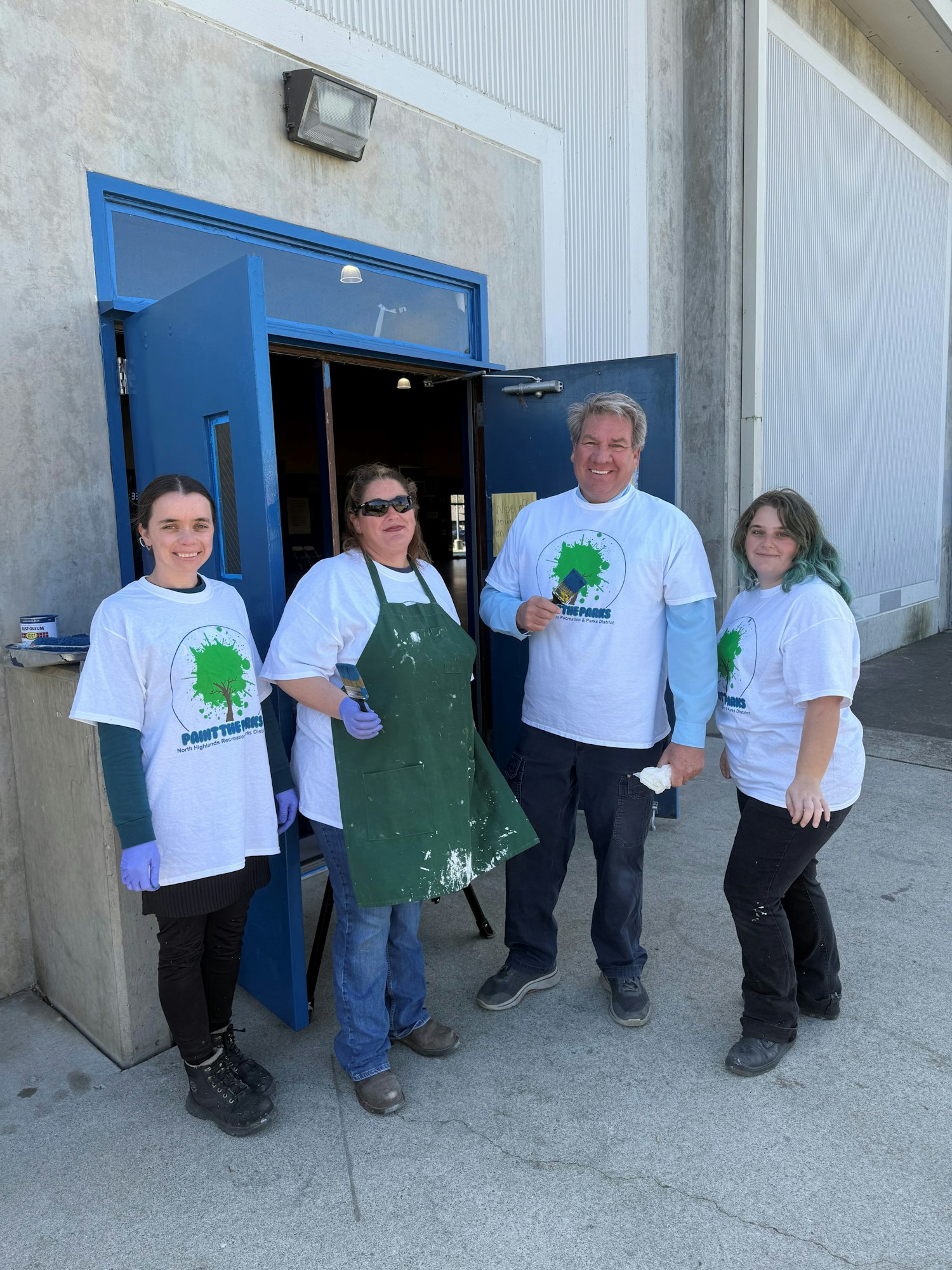 Four people in matching shirts stand smiling outside a blue door.