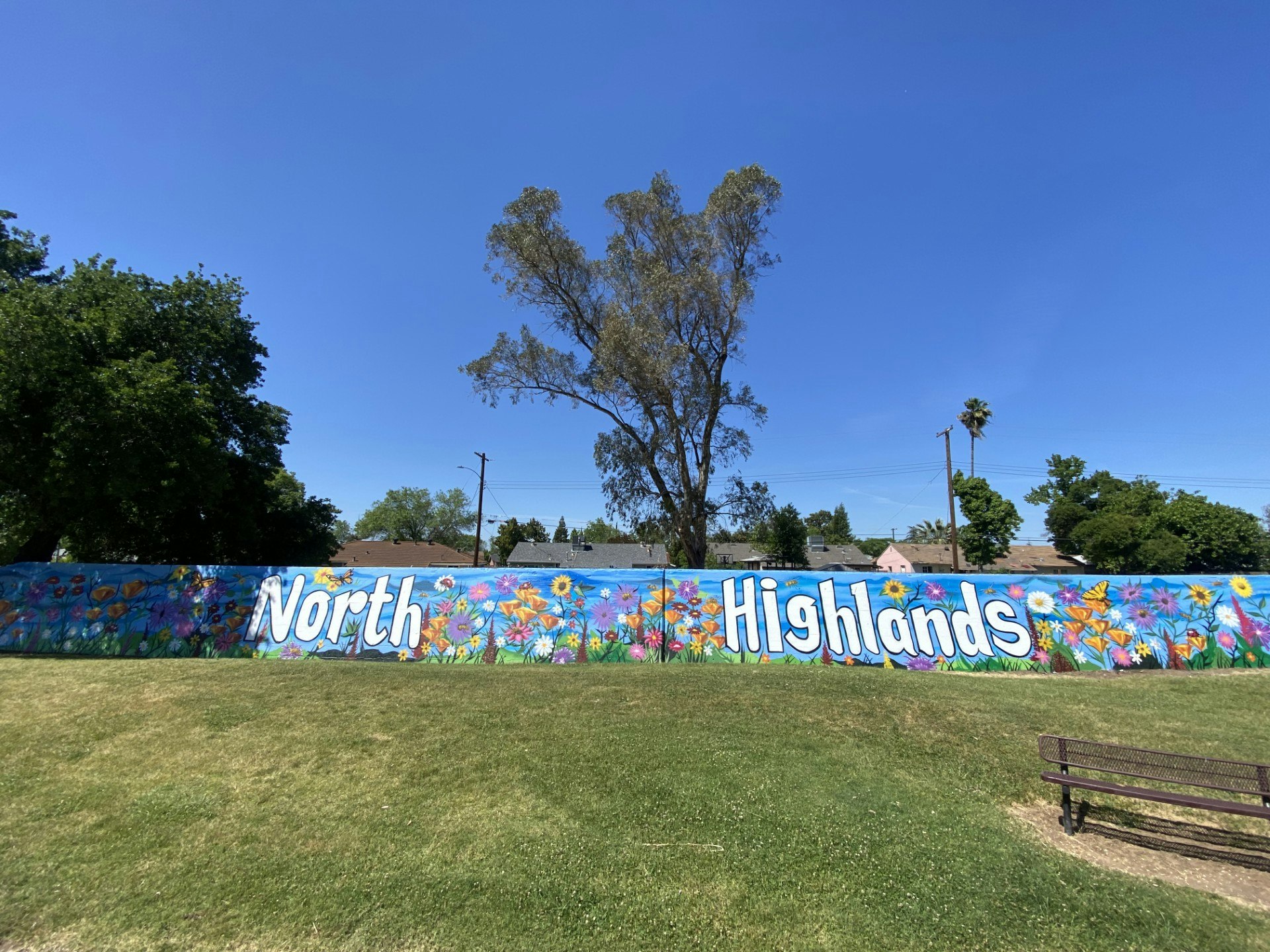 Colorful mural with "North Highlands" amidst flowers on a wall under blue sky.