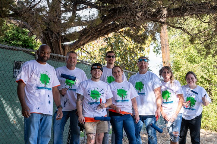 A group of people in matching T-shirts holding painting supplies outdoors.