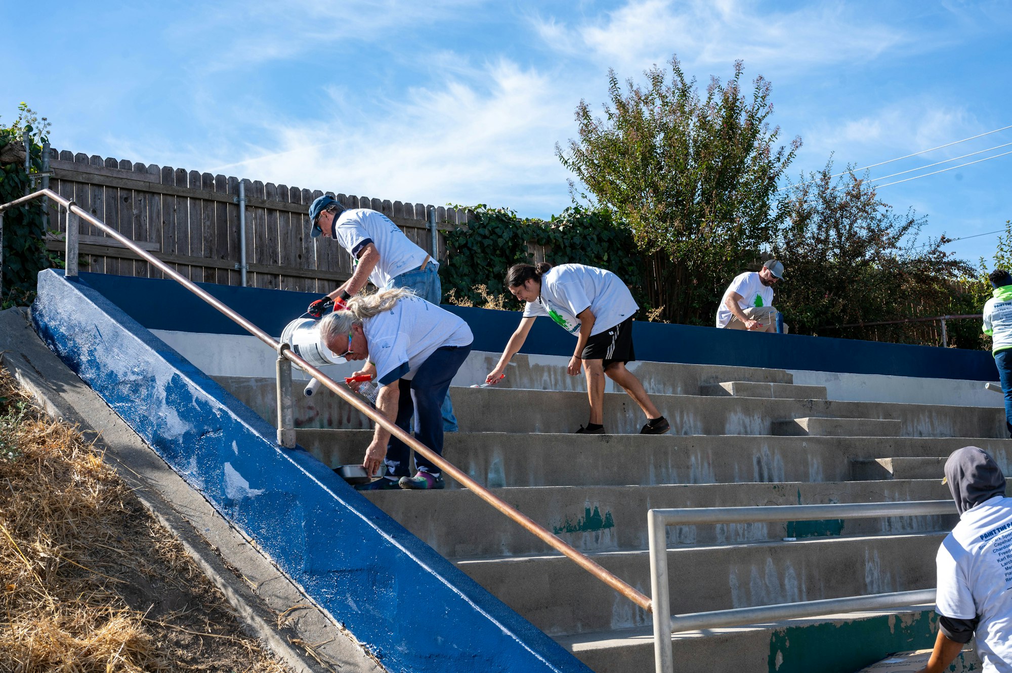 Volunteers are painting a staircase blue under a clear sky.