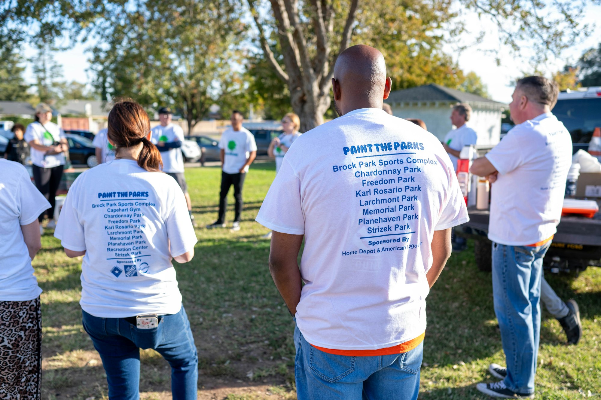 People with white T-shirts that say "PAINT THE PARKS" and list park names. Sponsor logos at the bottom.