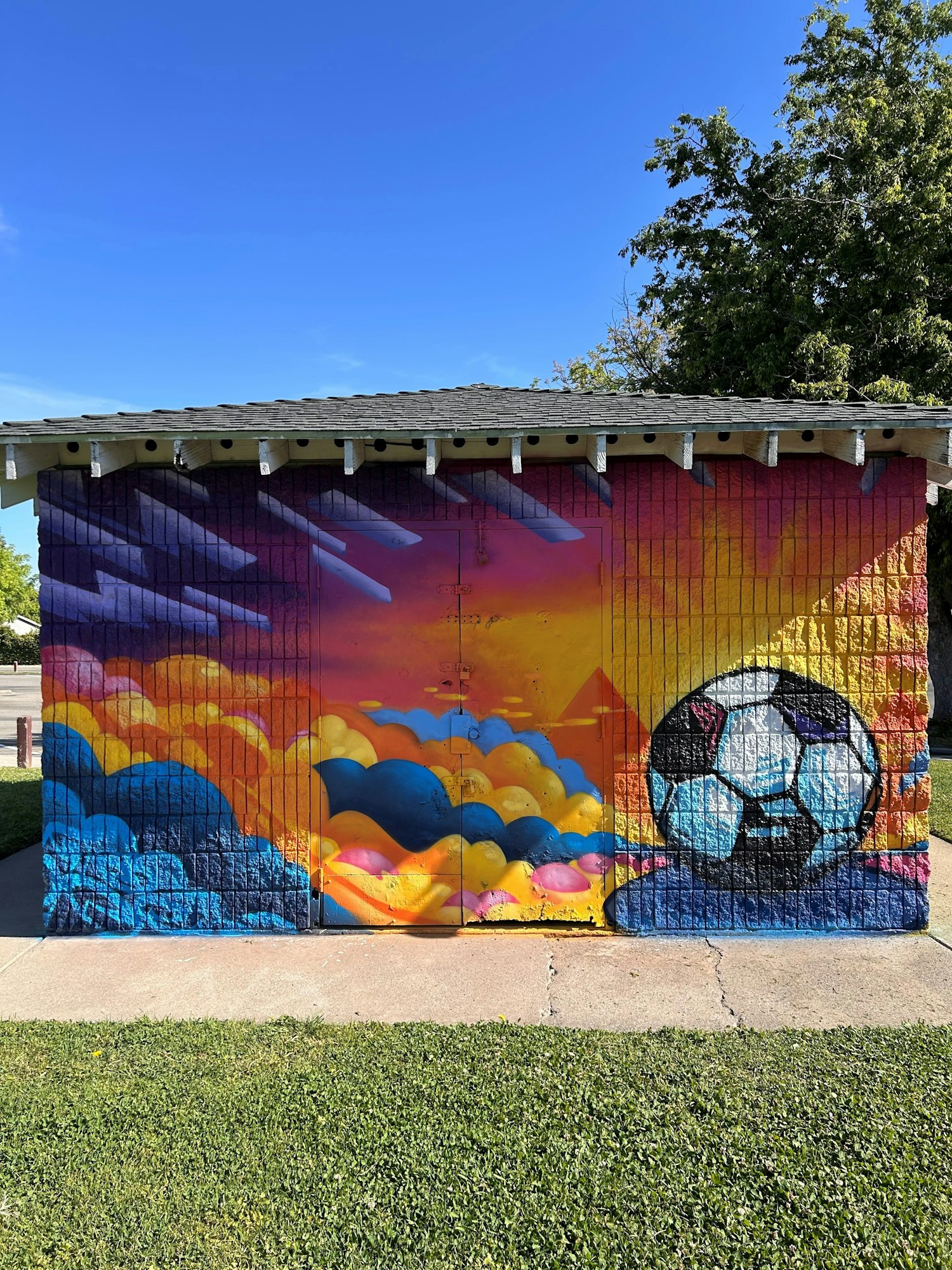 Colorful mural on a building wall featuring clouds and a soccer ball against a vibrant sky background.