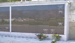 The image shows a memorial wall with dark panels, likely for commemorating individuals, adorned with flowers at the base.