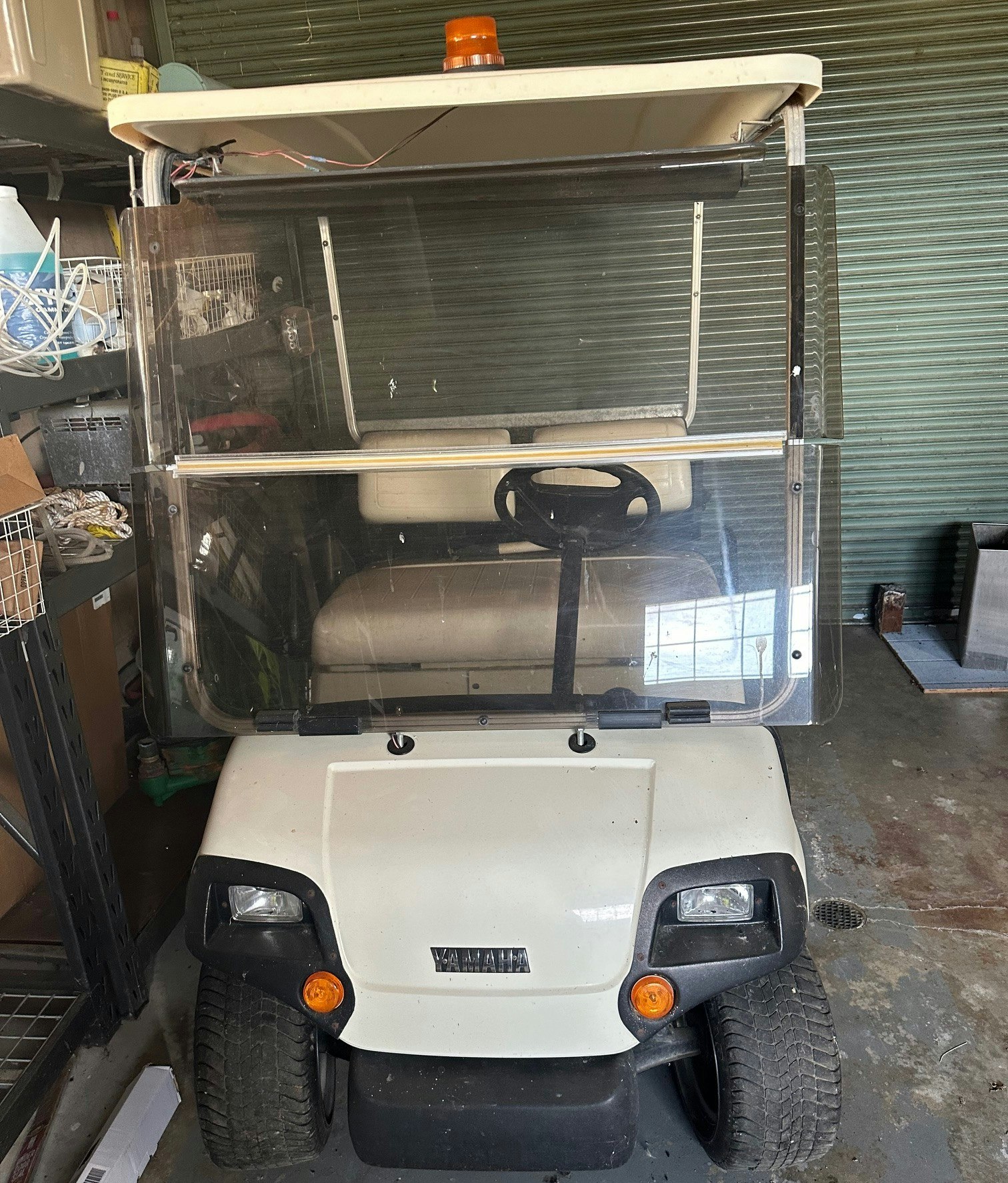 A white golf cart with an orange light on top, parked in a garage.