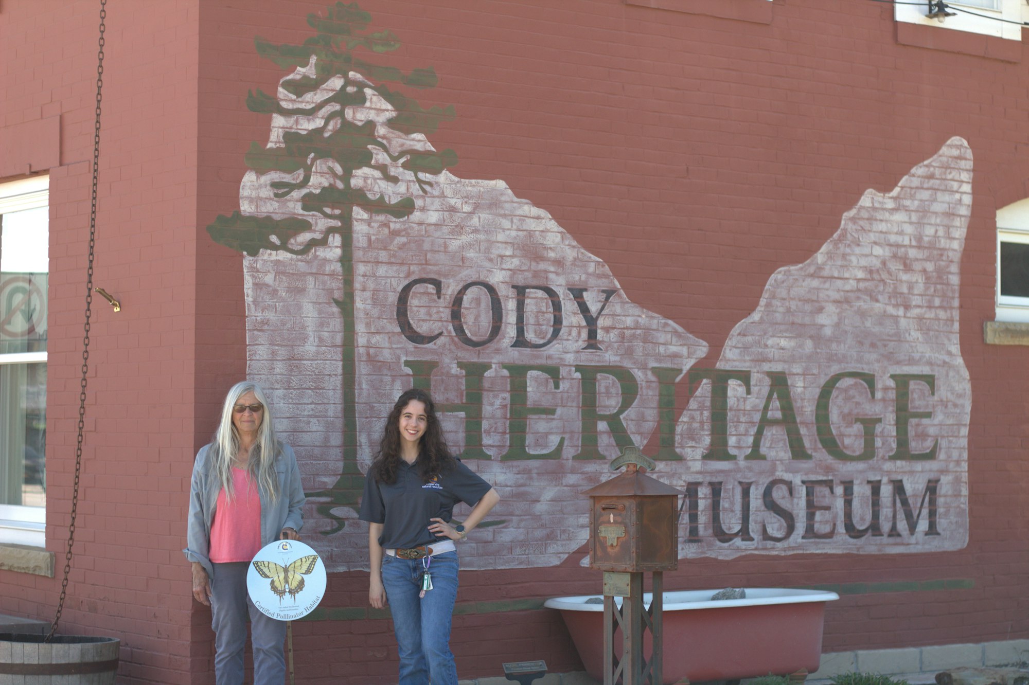 Two people stand in front of the Cody Heritage Museum mural.