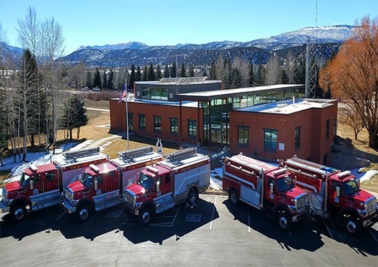 Fire station with trucks in front, mountains in the background.