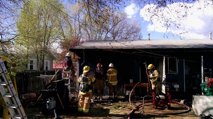 Firefighters working at the site of a house with signs of fire damage.