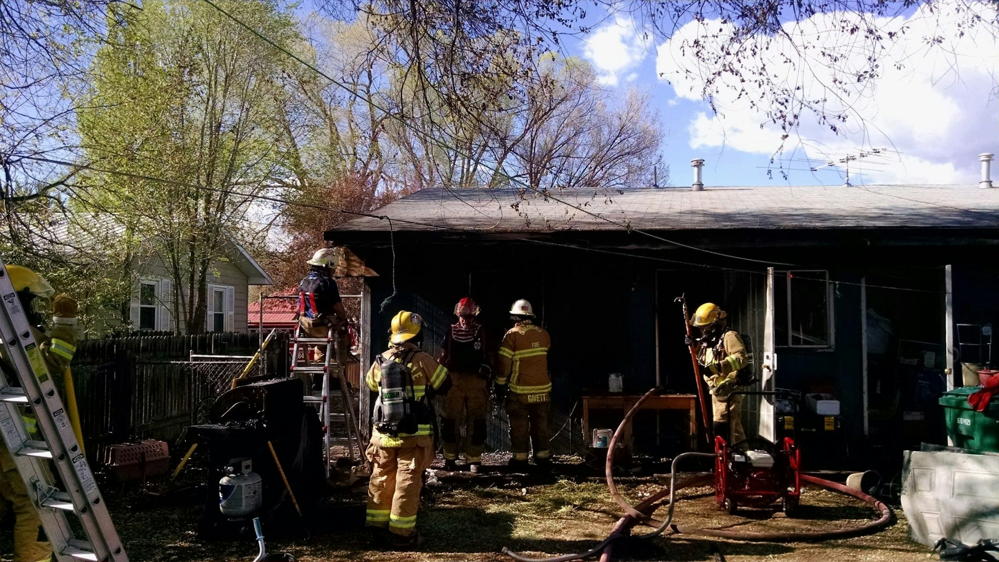 Firefighters working at the site of a house with signs of fire damage.