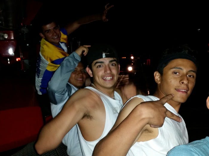 A group of young people posing and smiling, with someone in a yellow and blue jersey in the background.