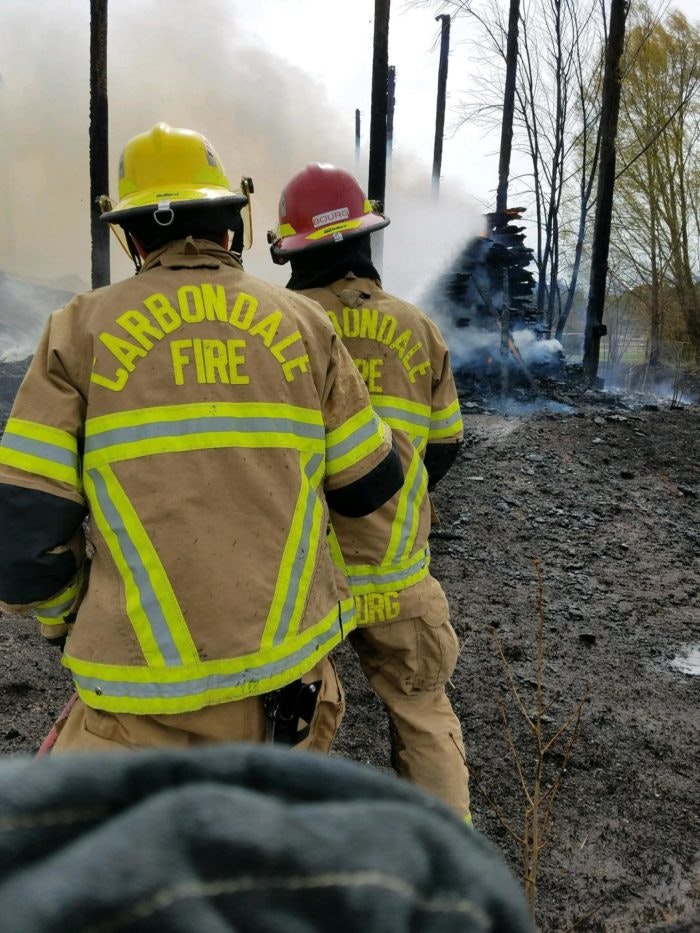 Two firefighters watching a controlled burn with smoke in the background.