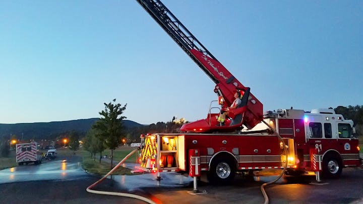 A fire truck with an extended ladder at dusk, firefighter at the controls.