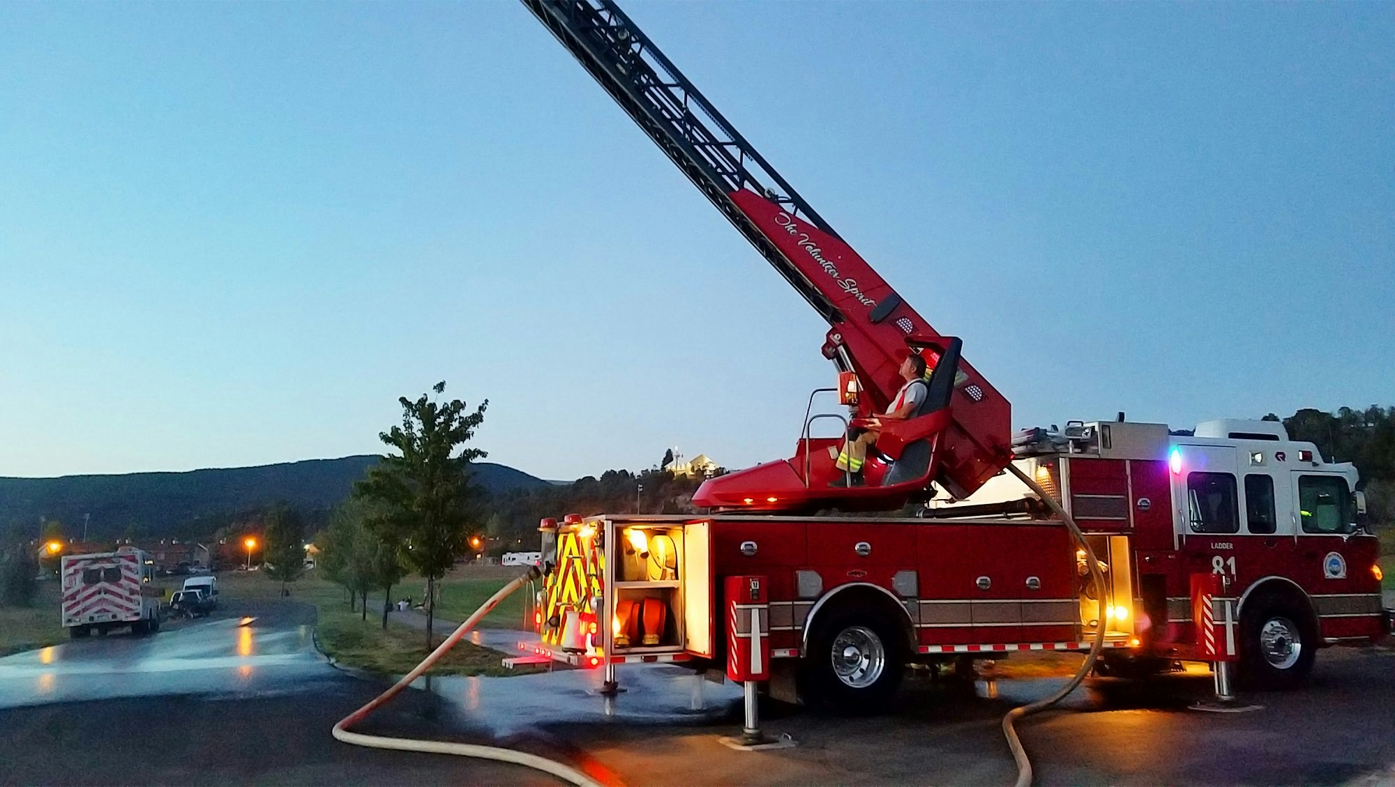 A fire truck with an extended ladder at dusk, firefighter at the controls.
