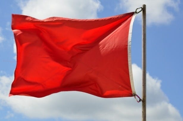 A red flag waving against a blue sky with clouds.