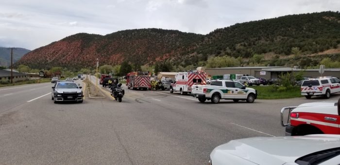 Emergency vehicles and personnel on a road, possibly responding to an incident, with a backdrop of mountains and overcast sky.