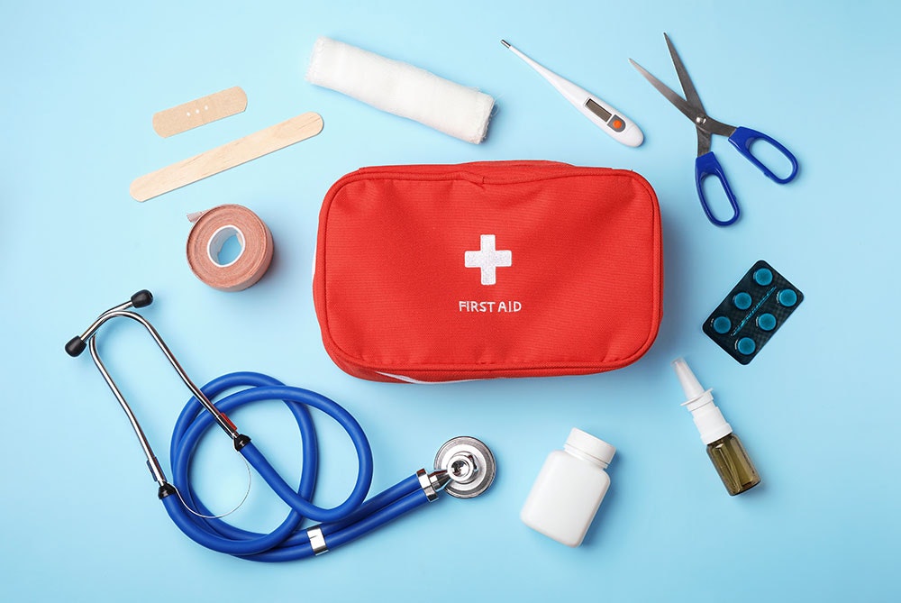 A first aid kit with medical supplies including a stethoscope, bandages, scissors, medicine, and a thermometer on a blue background.