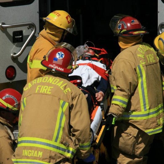 Firefighters in gear tending to an individual on a stretcher, with a fire truck in the background.
