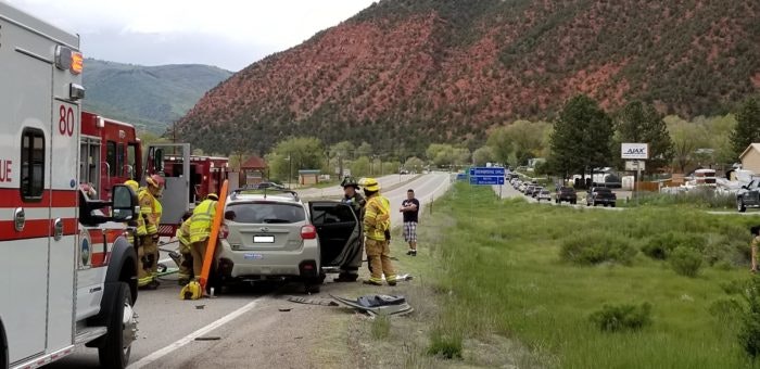 Emergency responders at a car accident scene near a road with hills in the background.