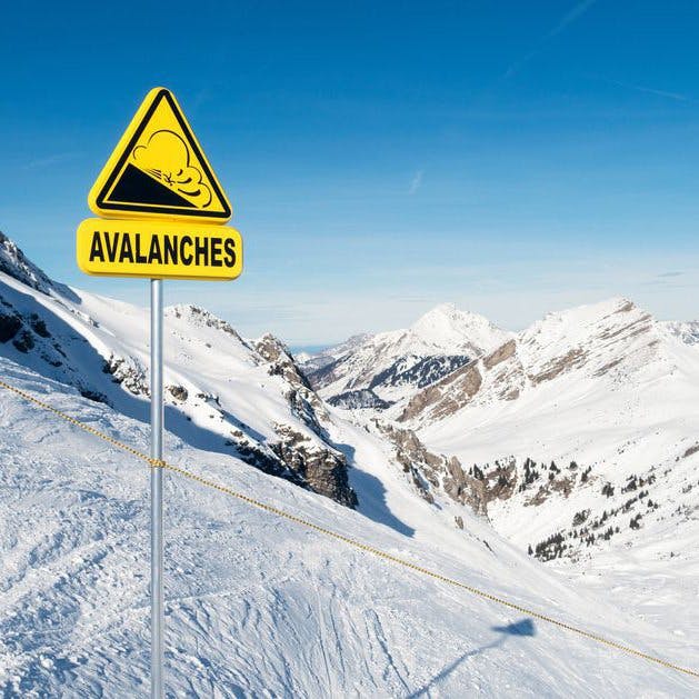 A yellow avalanche warning sign in a snowy mountain landscape.
