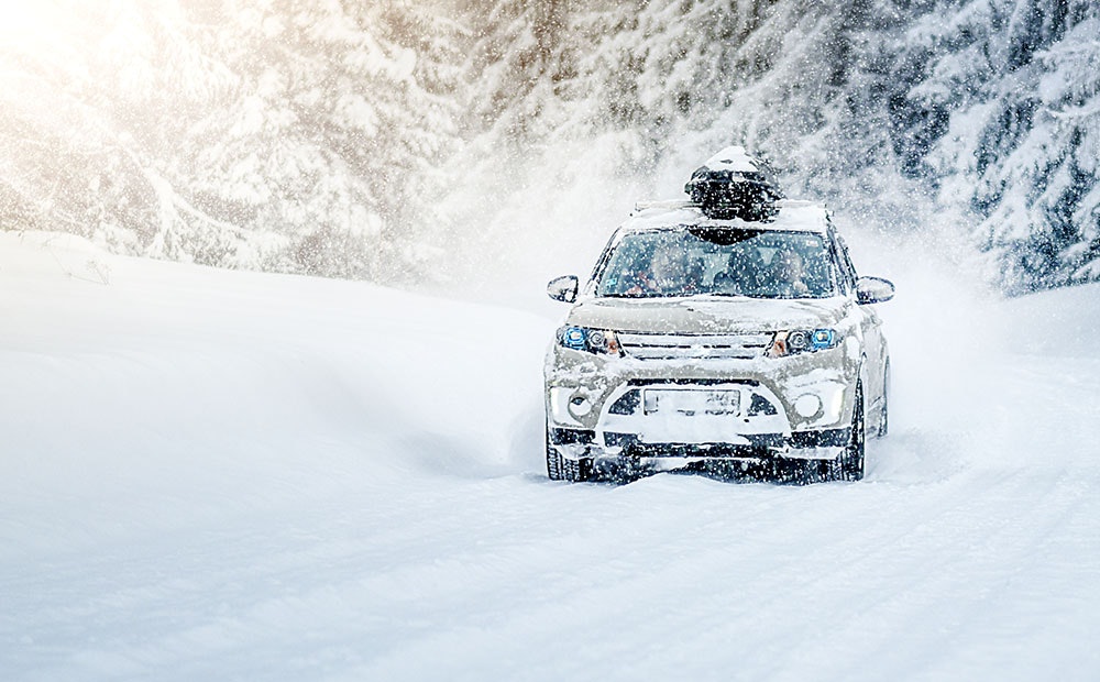 An SUV driving through a heavy snowstorm with a forest backdrop.