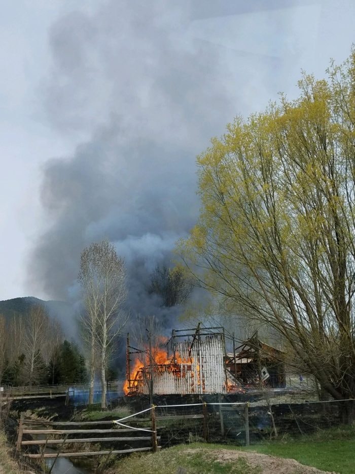 A building on fire with smoke, surrounded by trees under a cloudy sky.