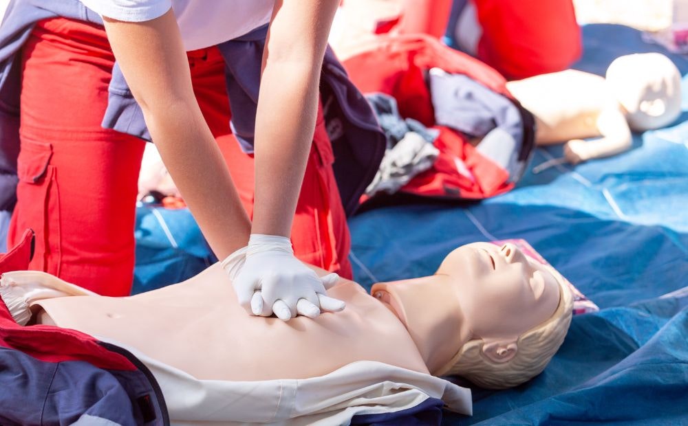 CPR training session with a manikin and a person wearing gloves performing chest compressions.