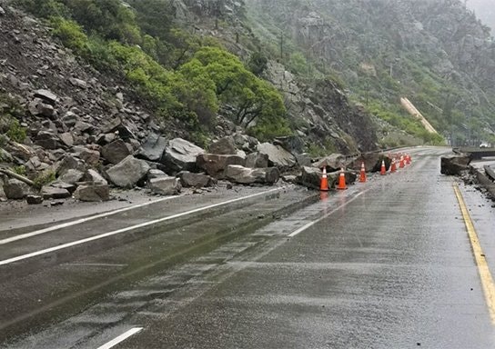 Rockslide on a wet road with traffic cones.