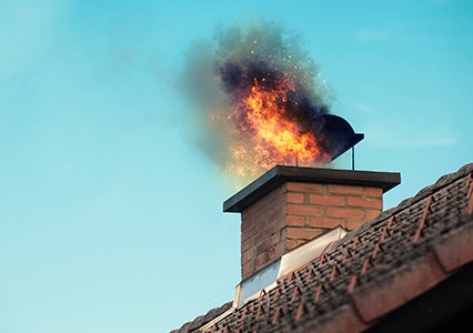 Chimney on a tiled roof with flames and smoke, indicating a chimney fire.