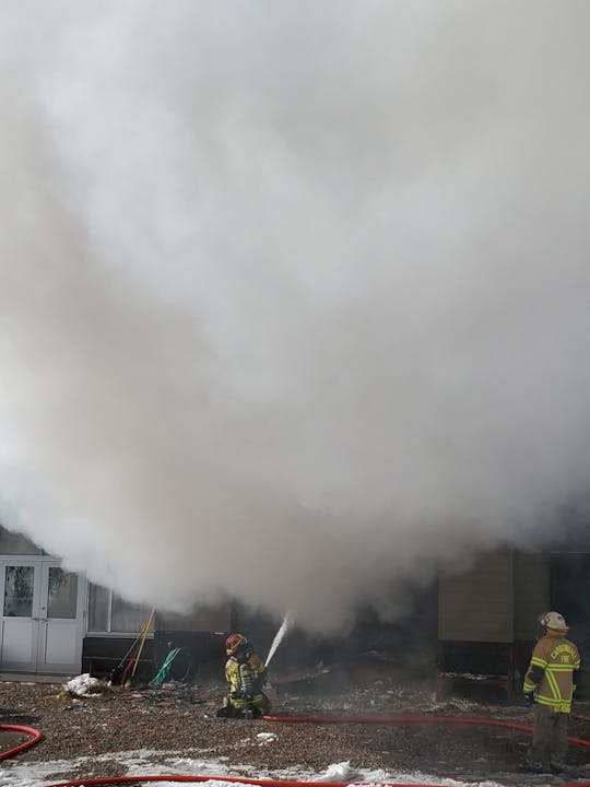 Firefighters battling a blaze with hoses; smoke billowing from a structure.