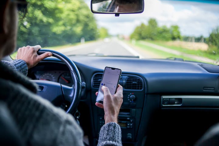 Driver holding a smartphone while driving on a road; an unsafe practice.