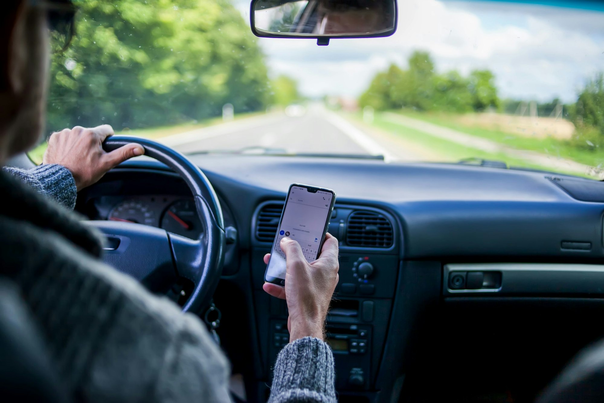 Driver holding a smartphone while driving on a road; an unsafe practice.