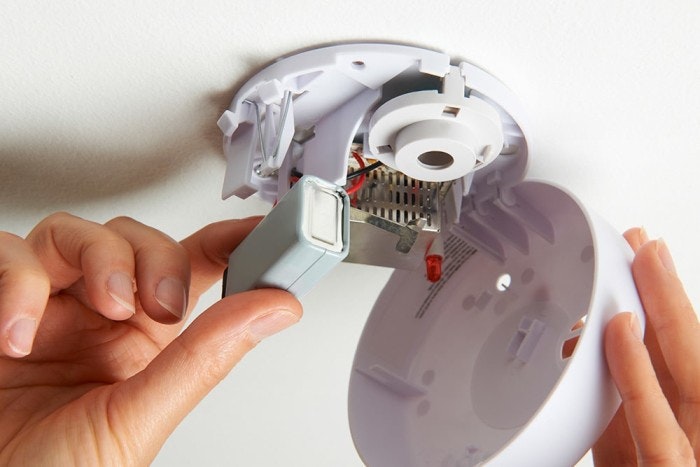 Hands installing a smoke detector on a ceiling.