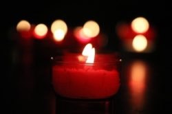 A lit red candle in focus with blurred candles in the background.