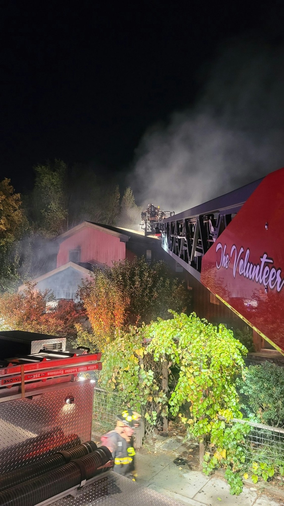 Firefighters at night working on a smoking structure beside a firetruck named "The Volunteer."