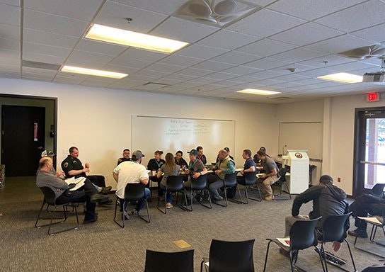 A group of people sitting in a classroom during a meeting or training session with papers in hand.