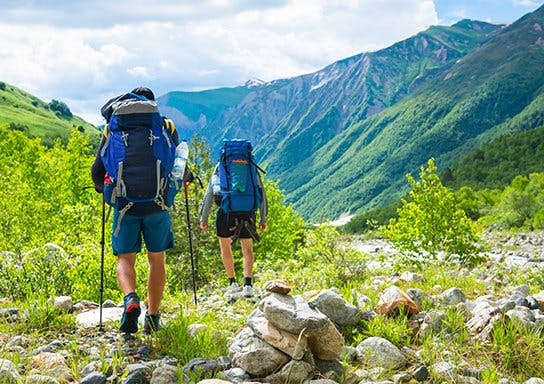 Two hikers with backpacks walk in the mountains.
