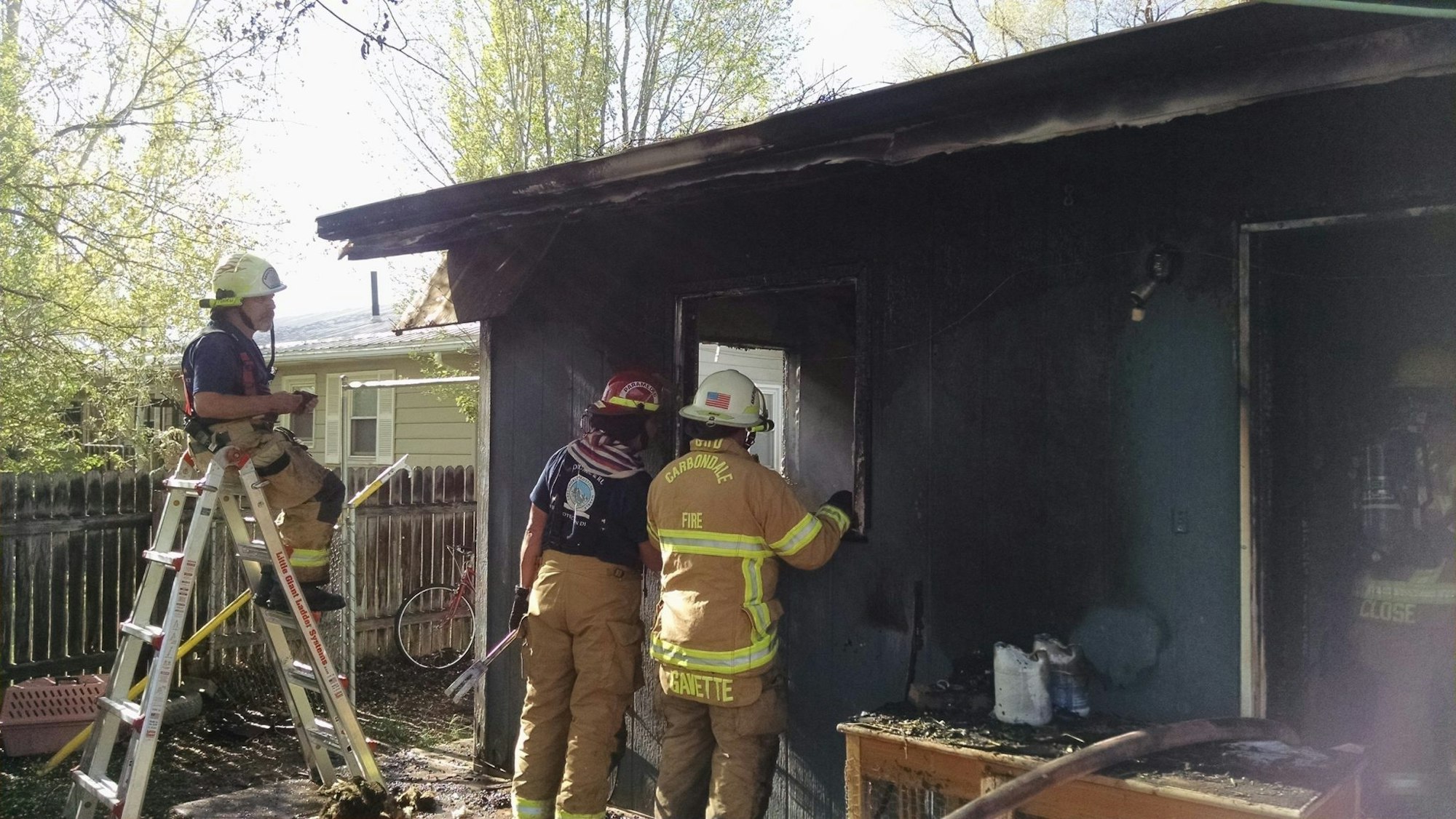 Firefighters examining a charred building post-fire with equipment, under daylight.