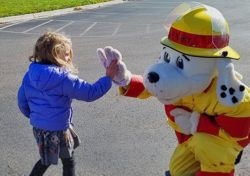 A child high-fiving a person in a firefighter-themed dog mascot costume.