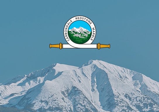 Snow-covered mountain with a circular emblem overlay featuring text, mountain graphics, and two horizontal bars.