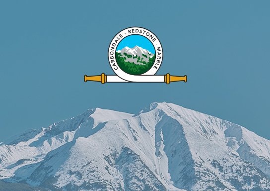 Snow-covered mountain with a circular emblem overlay featuring text, mountain graphics, and two horizontal bars.