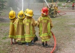 Children in firefighter gear using a hose, possibly during a fire safety demonstration or educational event.