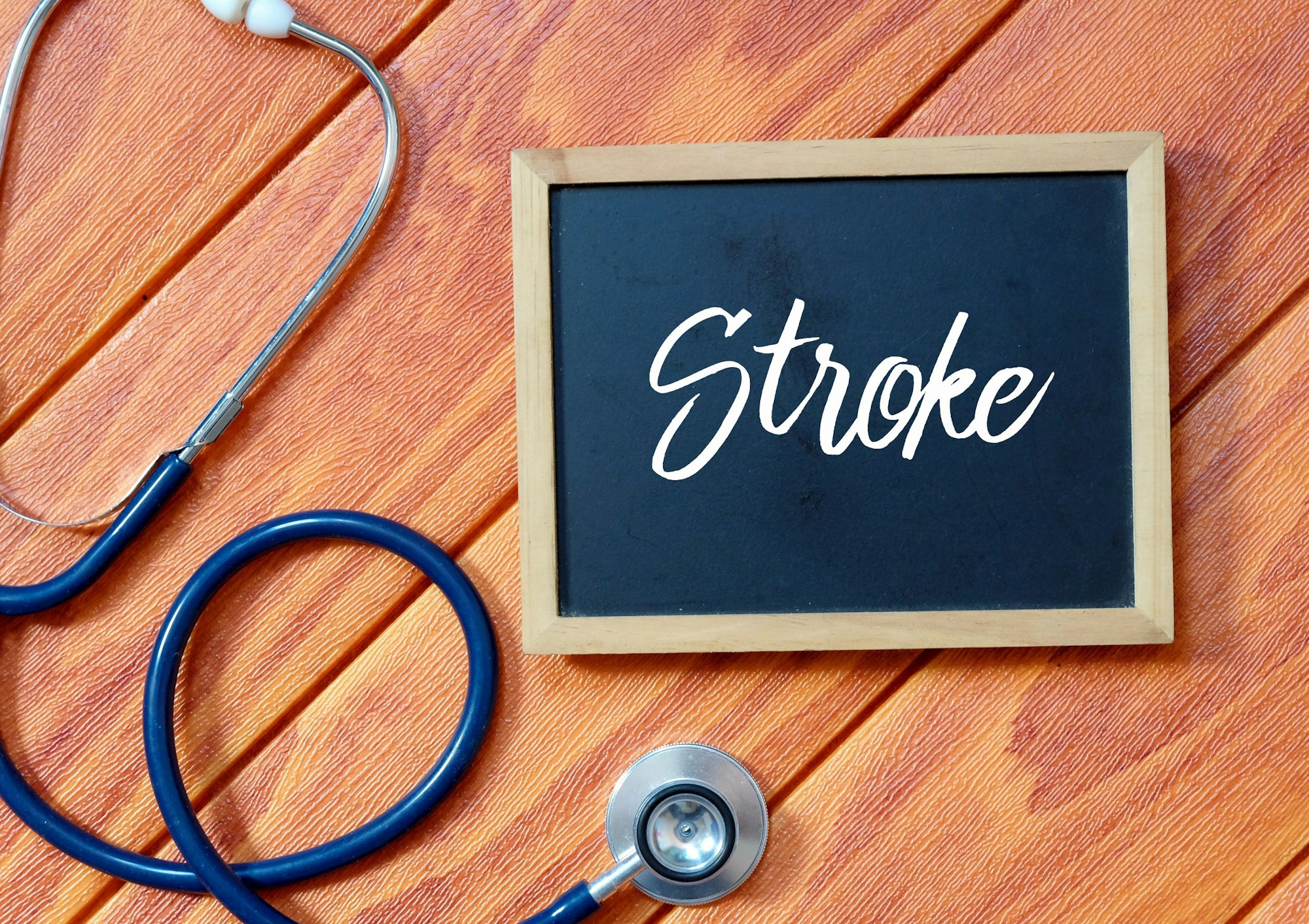 A chalkboard with "Stroke" written on it, alongside a stethoscope, on a wooden surface.