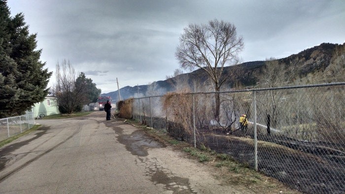 Rural road with a fence, firefighter, smoke, trees, and mountains.